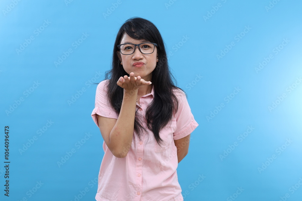 Adult asian woman keeps lips rounded, sends air kiss, blows muah , wears makeup, expresses romantic passionate feelings, models indoor. Adult asian woman keeps lips rounded, sends air kiss, blows muah , wears makeup, expresses romantic passionate feelings, models indoor.
