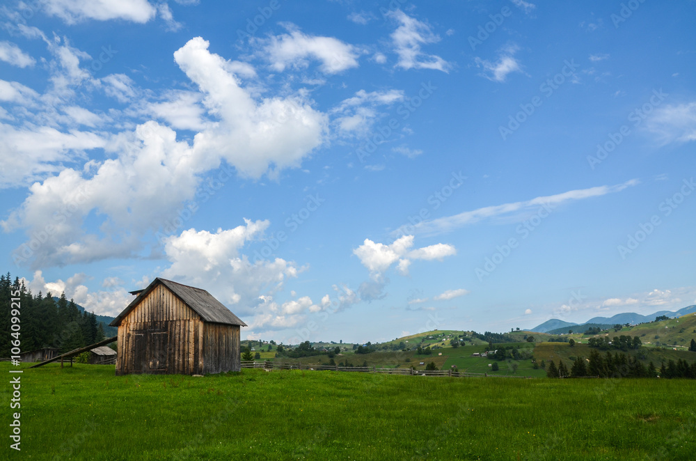 Picturesque rural landscape with rustic wooden barn situated in a lush green field, with rolling hills and mountains in the background. Carpathians, Ukraine Picturesque rural landscape with rustic wooden barn situated in a lush green field, with rolling hills and mountains in the background. Carpathians, Ukraine