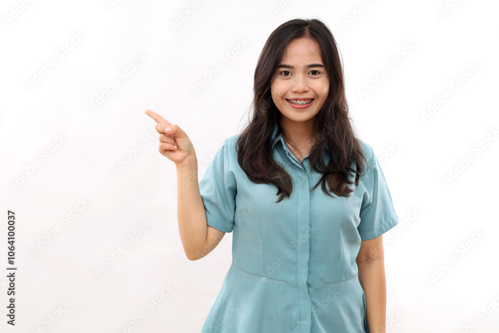 Beautiful Asian woman indicates aside, shows promo, gives advice, makes choice, smiles pleasantly, wears casual shirt, stands against white studio wall, tells about product details Beautiful Asian woman indicates aside, shows promo, gives advice, makes choice, smiles pleasantly, wears casual shirt, stands against white studio wall, tells about product details