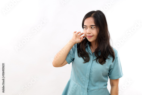 Indoor shot of pleasant looking young Asian woman keeps hand on hair focused away thinks about something wears shirt isolated over white background copy space for your advertising content