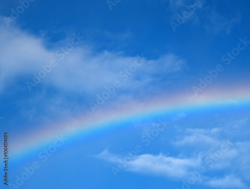 A vibrant rainbow arcs across a clear sky filled with fluffy white clouds during the afternoon sunlight after a brief rain shower