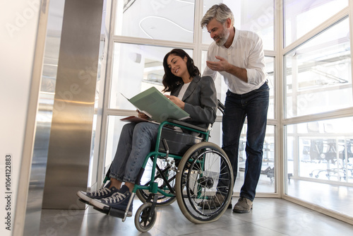 Man communicating with female in wheelchair near list in office hall