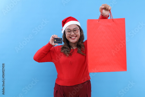 Young asian woman holding credit card and christmas gift bag, isolated on blue background photo