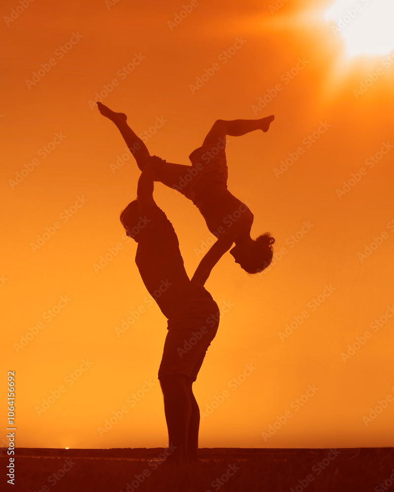 Young adult sports couple doing acro yoga exercises. Silhouette couple practicing yoga at sunset. Slim woman, man do acroyoga. sporty healthy pair doing acrobatic yoga at sunrise. female stand on back Young adult sports couple doing acro yoga exercises. Silhouette couple practicing yoga at sunset. Slim woman, man do acroyoga. sporty healthy pair doing acrobatic yoga at sunrise. female stand on back