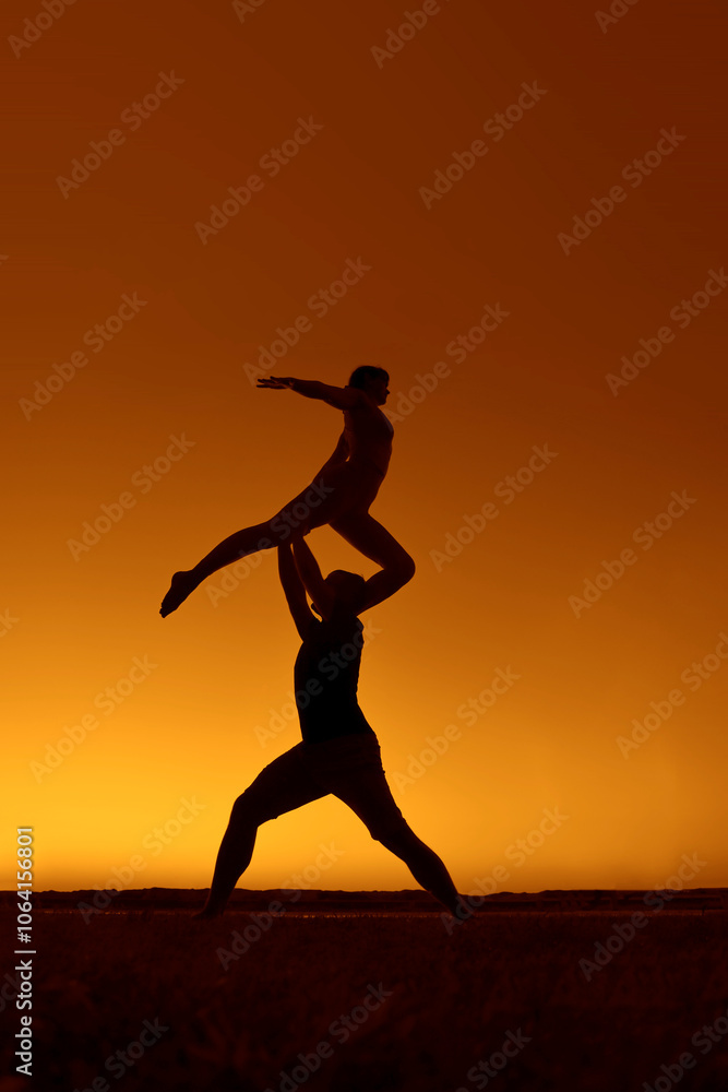 Young adult sports couple doing acro yoga exercises. Silhouette couple practicing yoga at sunset. woman, man do acroyoga. sporty healthy pair doing acrobatic yoga at sunrise. female stand on shoulder Young adult sports couple doing acro yoga exercises. Silhouette couple practicing yoga at sunset. woman, man do acroyoga. sporty healthy pair doing acrobatic yoga at sunrise. female stand on shoulder
