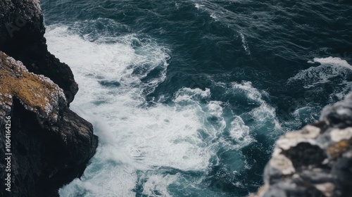 A close-up view of white ocean waves crashing against rugged dark grey cliffs.