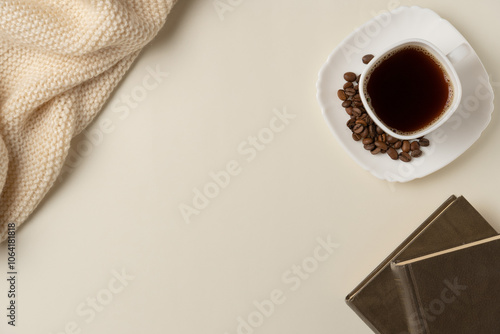 Cup of coffee with coffee beans, books and scarf on beige background. Copy space. Flat lay, top view