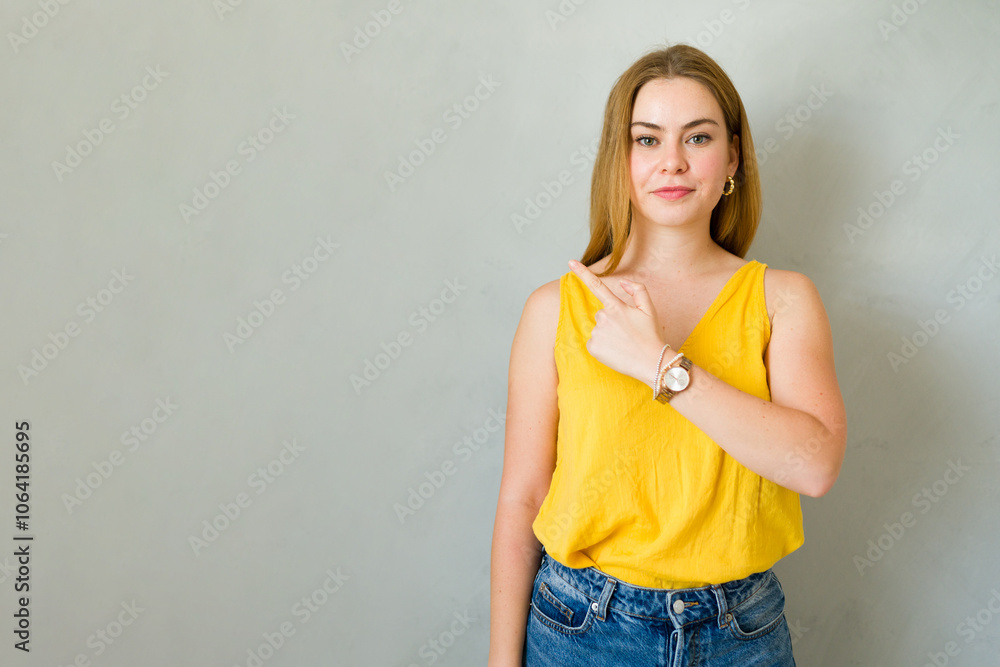 Cute young woman is gesturing to her right with her index finger against a gray backdrop Cute young woman is gesturing to her right with her index finger against a gray backdrop