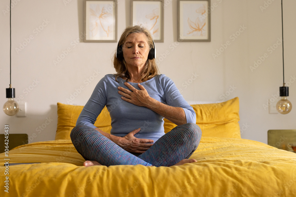 senior woman meditating on bed with headphones, practicing mindfulness at home senior woman meditating on bed with headphones, practicing mindfulness at home