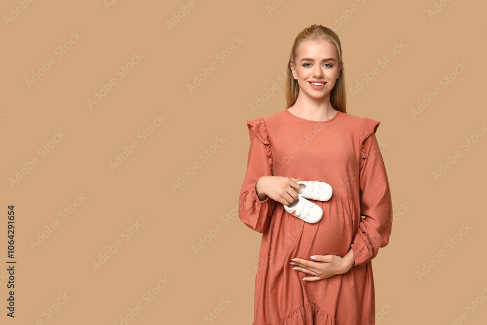 Beautiful happy pregnant woman with baby shoes on brown background Beautiful happy pregnant woman with baby shoes on brown background