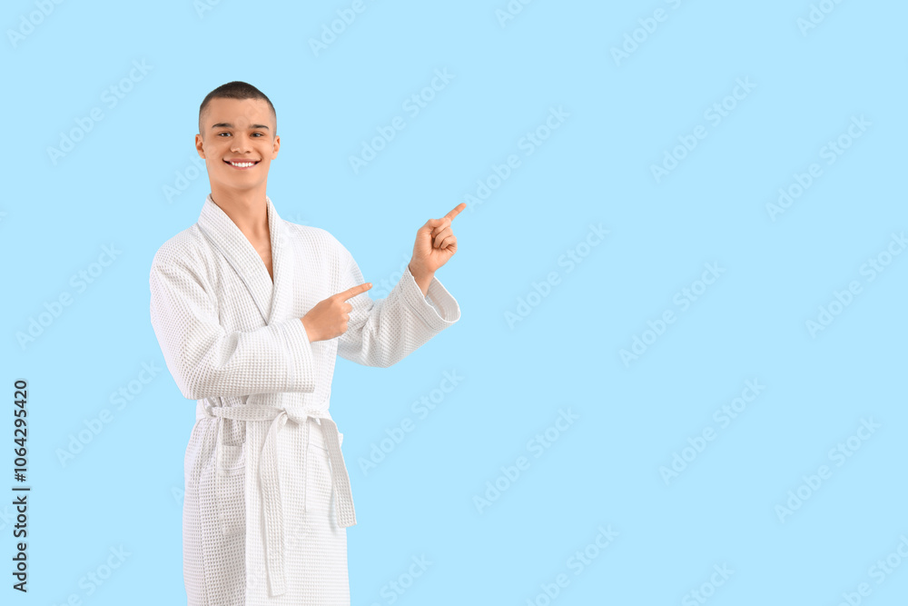 Teenage boy in bathrobe pointing at something on blue background Teenage boy in bathrobe pointing at something on blue background