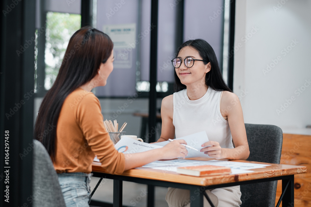 Two women having a professional discussion in a modern office setting, exchanging documents and ideas. Two women having a professional discussion in a modern office setting, exchanging documents and ideas.
