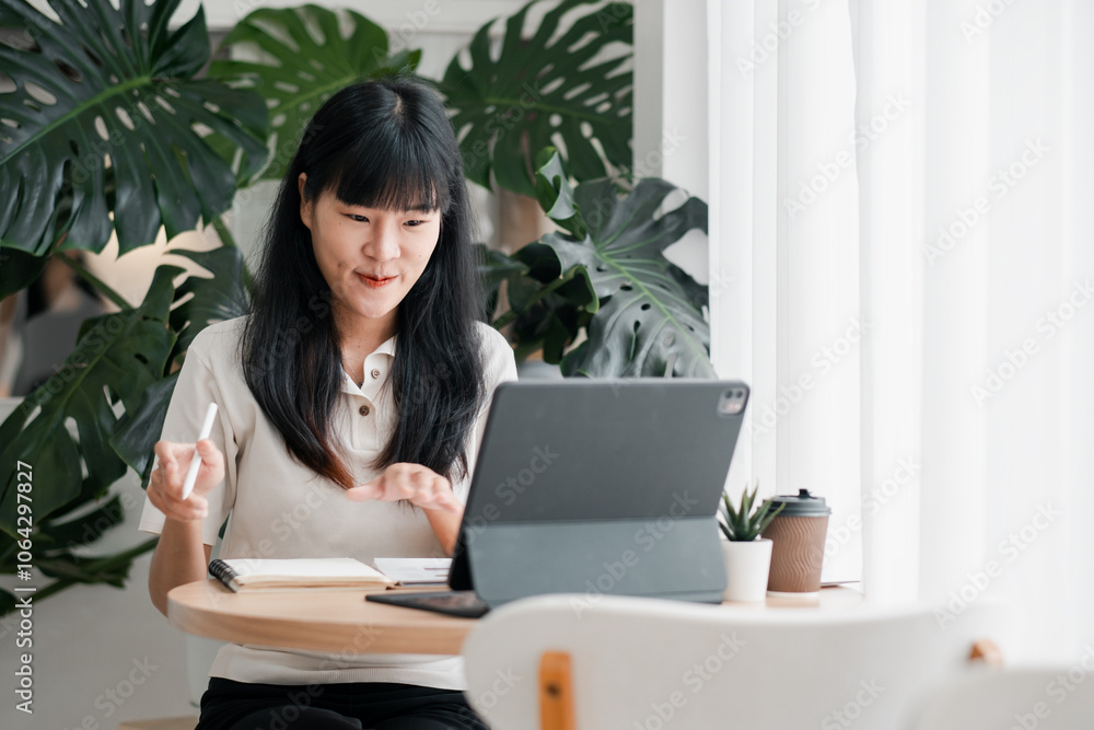 A young woman using a tablet and taking notes at a home office desk, surrounded by lush green plants and bright natural light. A young woman using a tablet and taking notes at a home office desk, surrounded by lush green plants and bright natural light.