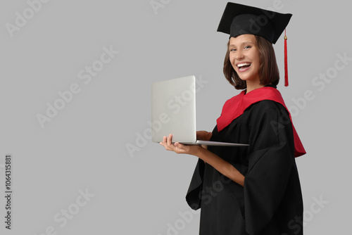 Female graduating student with laptop on grey background photo