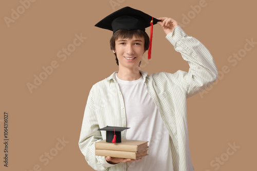 Male graduating student with books on beige background