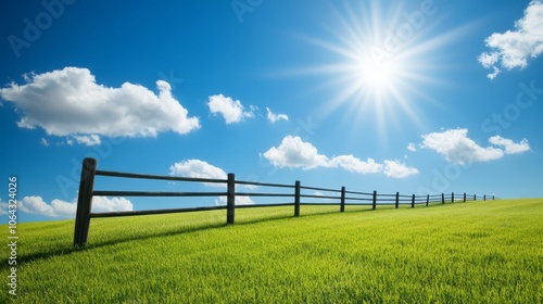 Picturesque countryside scene, wooden fence meandering through a lush green field under brilliant blue sky