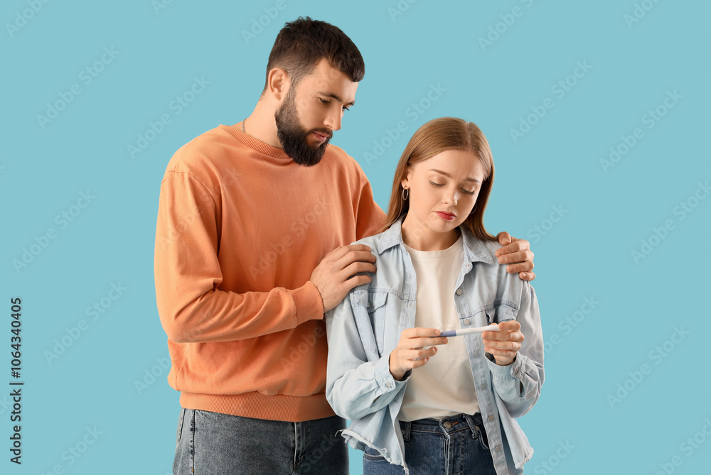 Upset young couple with pregnancy test on blue background Upset young couple with pregnancy test on blue background