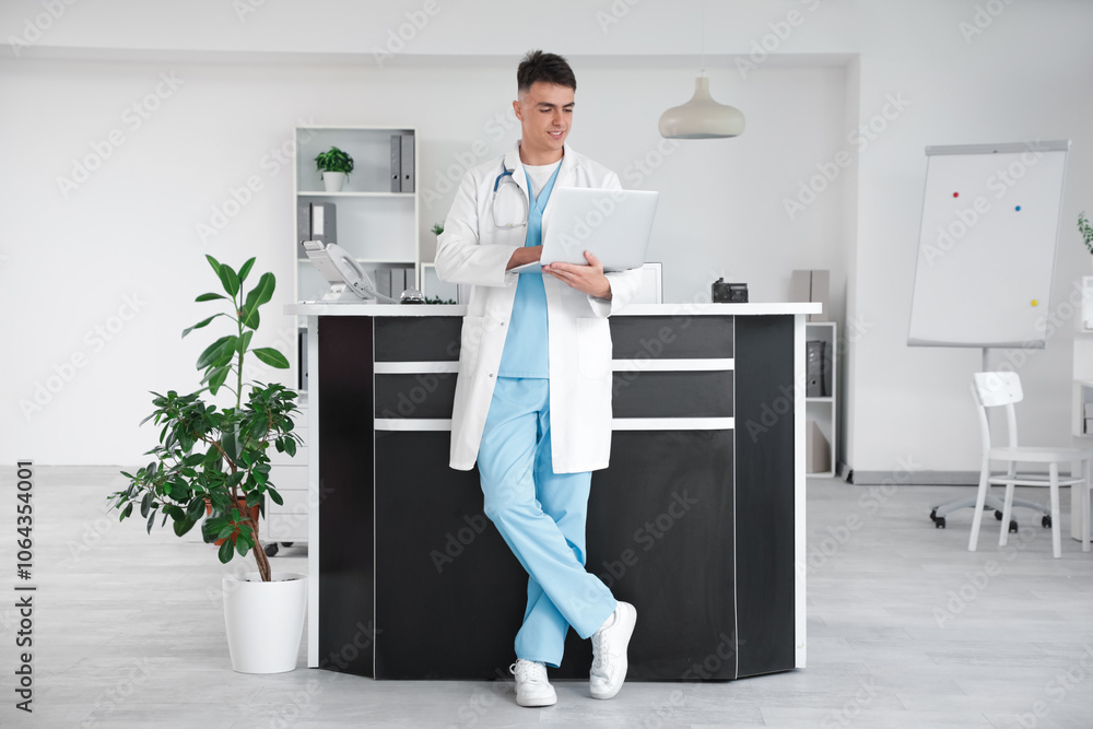 Male medical intern working with laptop near reception in clinic Male medical intern working with laptop near reception in clinic