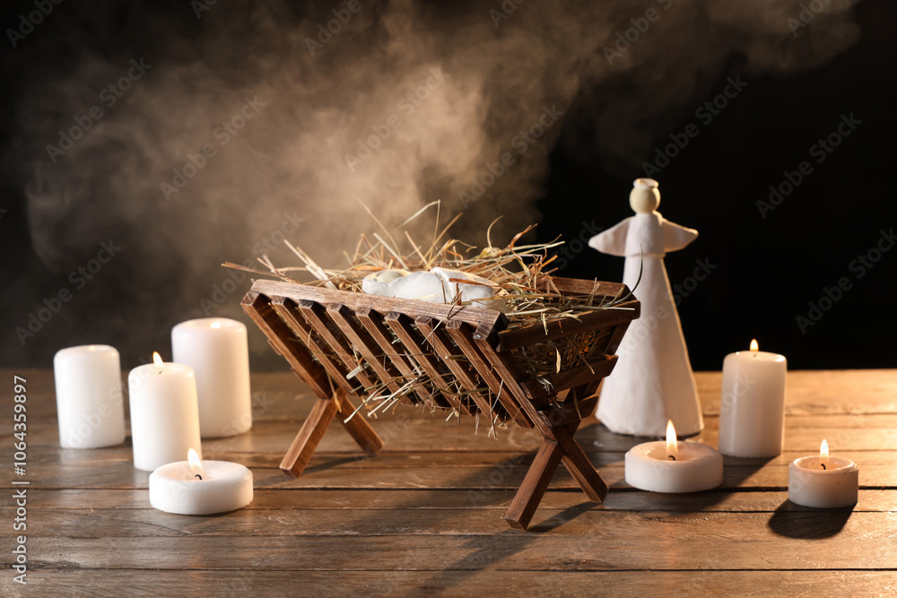 Naklejka premium Manger with baby Jesus, angel and burning candles on table against dark background