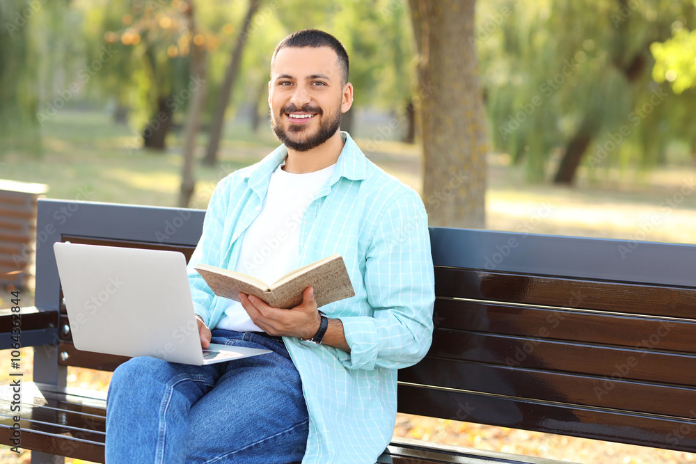 Young man with notebook using laptop on bench in park Young man with notebook using laptop on bench in park