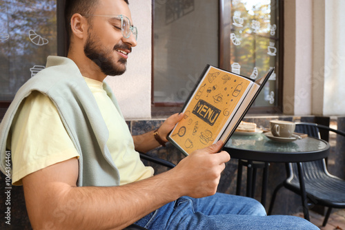 Young man reading menu at t...