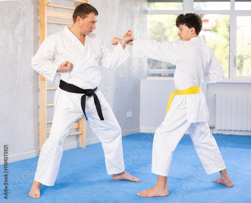 Adult man and teenage boy in kimono practicing karate fighting in gym