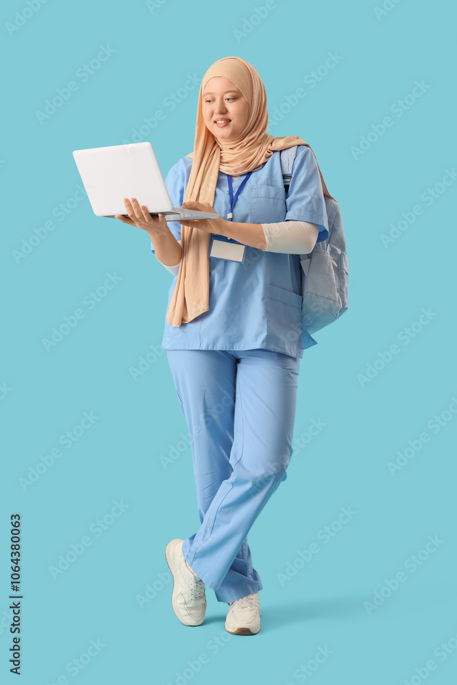 Female Muslim medical student with laptop on blue background Female Muslim medical student with laptop on blue background