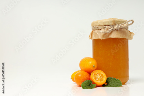 Fresh kumquat fruits and glass jar with jam on white background, space for text