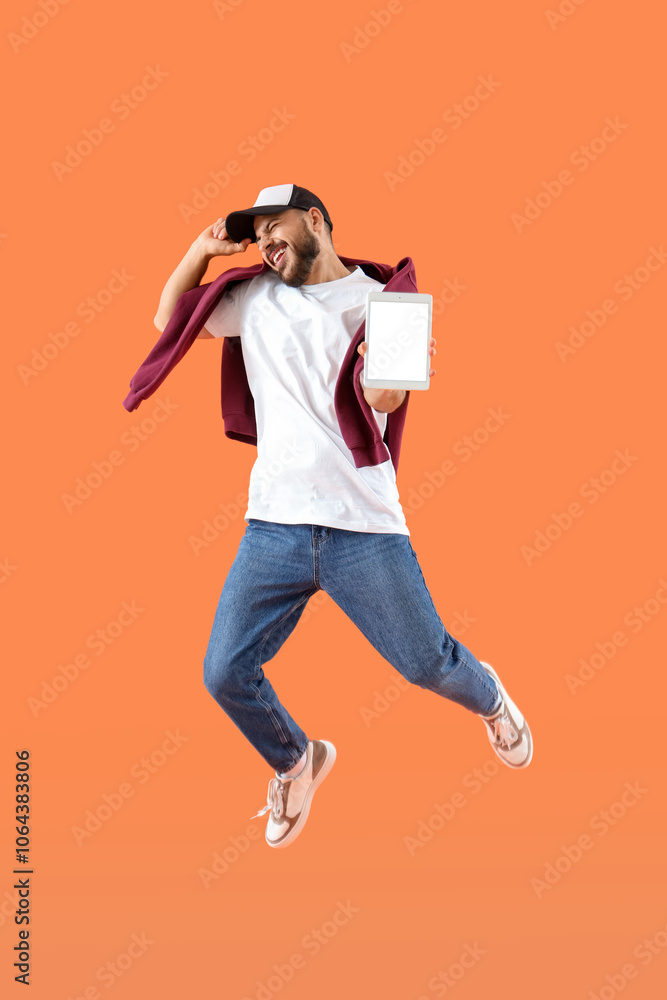 Young man with blank tablet computer jumping on orange background Young man with blank tablet computer jumping on orange background