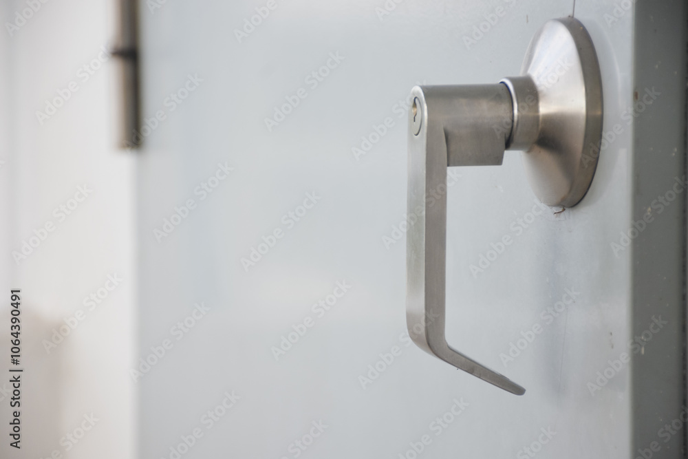 Close-up of a door handle. The door handle is made of metal and has a modern, sleek design. The handle is attached to the door and appears to be made of a smooth, light-colored material. Close-up of a door handle. The door handle is made of metal and has a modern, sleek design. The handle is attached to the door and appears to be made of a smooth, light-colored material.