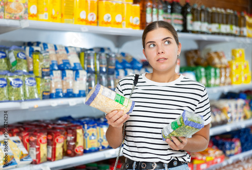 Young girl stands in cereal section of supermarket and chooses pack of peas photo