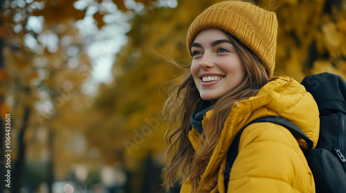 Cheerful young woman in a yellow jacket and beanie enjoying a sunny autumn day in the park