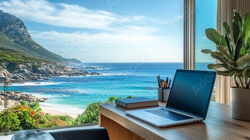 Laptop on a desk with a view of the ocean and mountains.