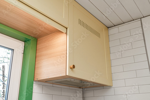 Fragment of upper kitchen cabinets with yellow facades and wooden knobs installed on tiled wall around window