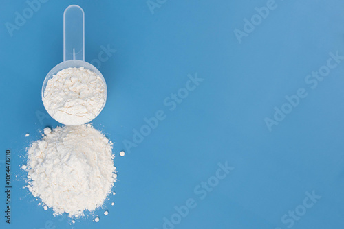 White protein powder, collagen supplement, or baby formula in measuring scoop on blue background. Concept of health, wellness, child food nutrition, fitness, skincare, and childcare. 