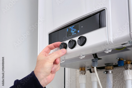A man sets the temperature on a modern digital gas boiler in a house.