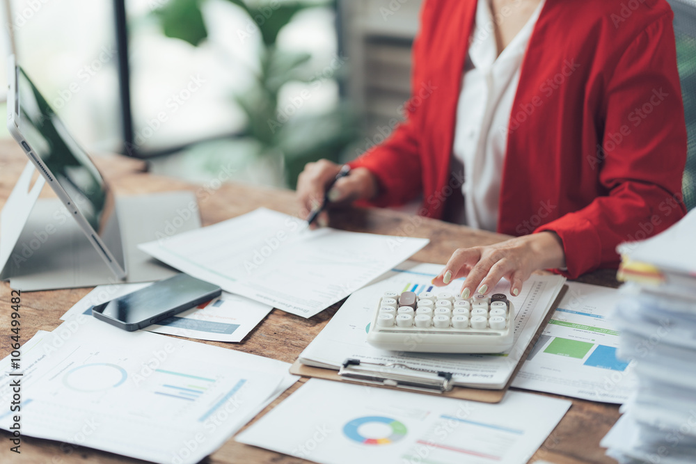 Focused Businesswoman at Desk: A detail-oriented shot of a businesswoman meticulously working at her desk, surrounded by paperwork, a calculator, and digital devices. Focused Businesswoman at Desk: A detail-oriented shot of a businesswoman meticulously working at her desk, surrounded by paperwork, a calculator, and digital devices.