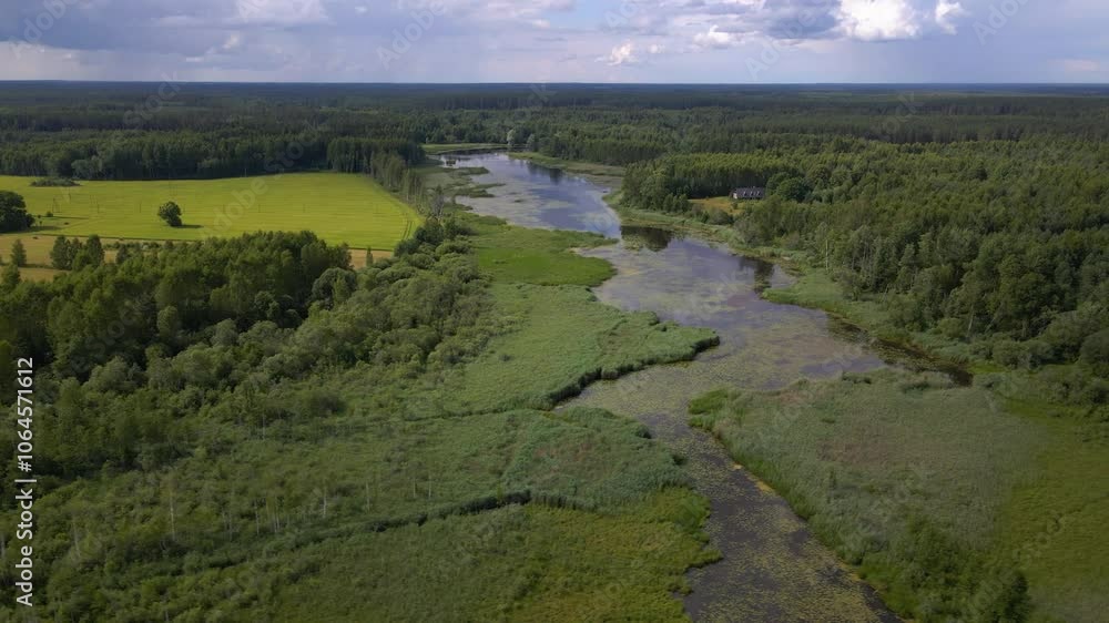 Drone flies sideways over a river that resembles a swamp. It is surrounded by lush greenery and open fields creating a serene landscape. Drone flies sideways over a river that resembles a swamp. It is surrounded by lush greenery and open fields creating a serene landscape.