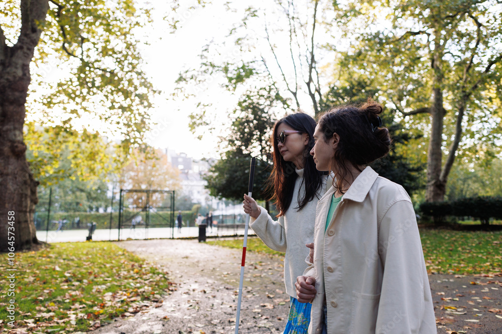 Young woman helping blind friend walking in park using white cane Young woman helping blind friend walking in park using white cane