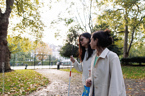Photos Young woman helping blind friend walking in park using white cane