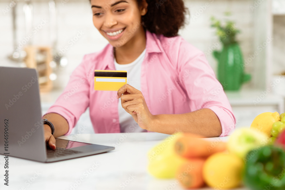 Ordering Food Online. Smiling black girl with laptop and credit card purchasing grocery delivery from internet in kitchen