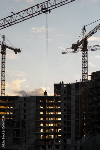 Bild auf Leinwand Cranes operate at a construction site during sunset, with workers visible on the