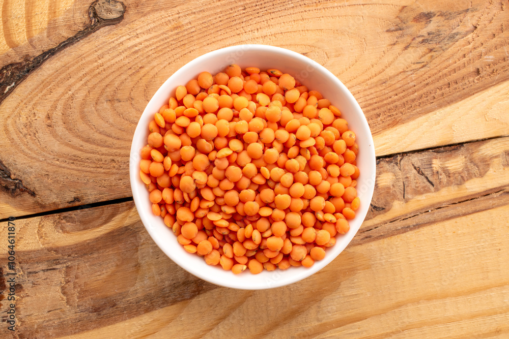 Raw red lentils in a ceramic dish on a wooden table, macro, top view. Raw red lentils in a ceramic dish on a wooden table, macro, top view.