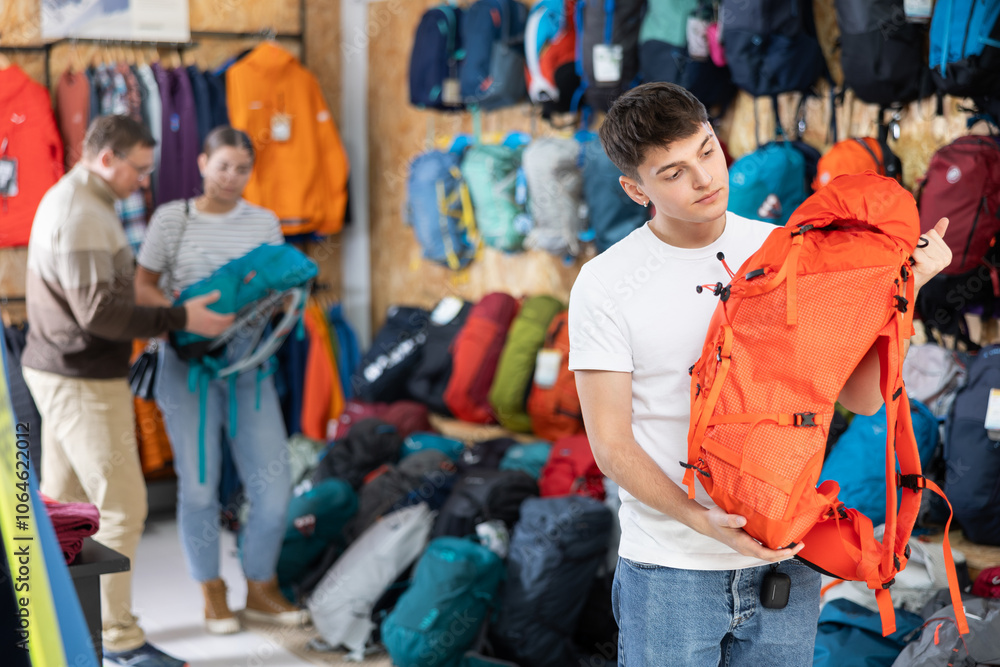 Obraz premium Guy view decide on summer backpack for walking tour. Buyer check reliability of locks and zippers, capacity of pockets and number of compartments and compartments.