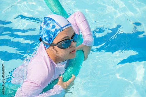 Girl with Down syndrome bathing in the pool on a summer day. inclusion, trisomy 21. wears diving goggles and a protective shirt.