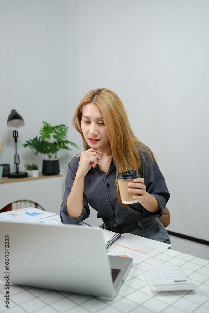 A woman is sitting at a desk with a laptop and a cup of coffee A woman is sitting at a desk with a laptop and a cup of coffee