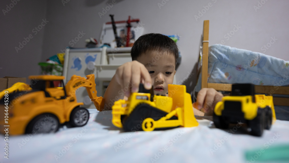 Cheerful young boy sitting and smiling while playing with a yellow truck at bedroom Cheerful young boy sitting and smiling while playing with a yellow truck at bedroom