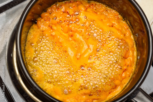 Boiling sea buckthorn berries with sugar in a saucepan for making jam.