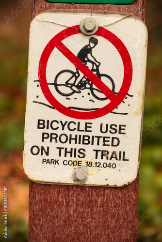 Close up of a bicycle use prohibited sign by a trail, note of a park code.  photo