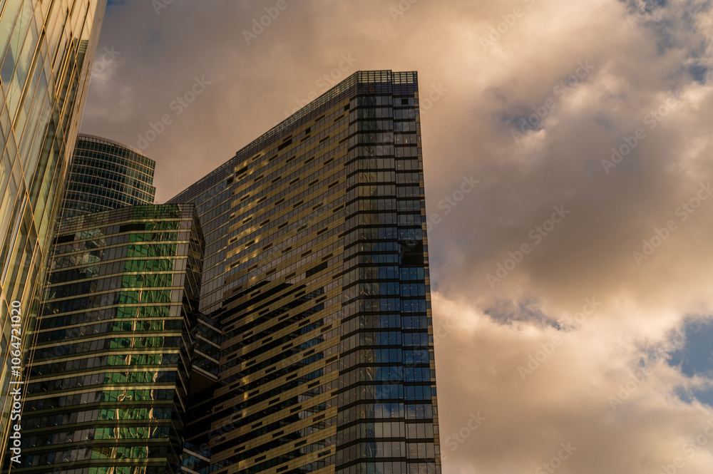 Fototapeta premium Skyscrapers in business district against blue sky. Looking Up high-rise office buildings. Evening time, sunset. Orange, yellow and gold shades of color. Angled view.